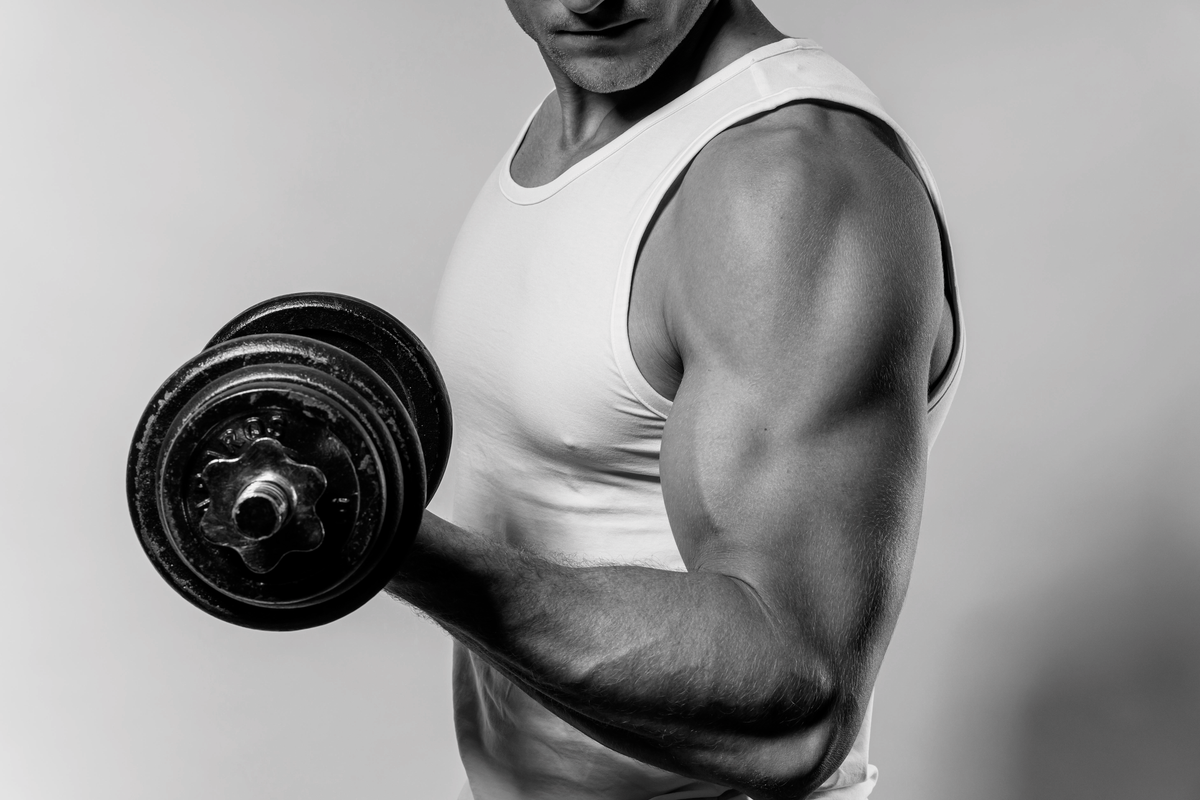 Fit man in a tank top flexing his bicep while holding a weight